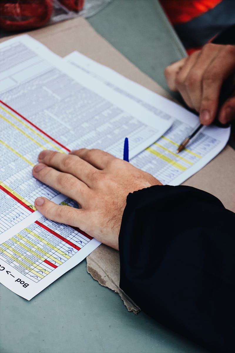 Hands with pen analyzing spreadsheets at a desk, focusing on data and statistics.